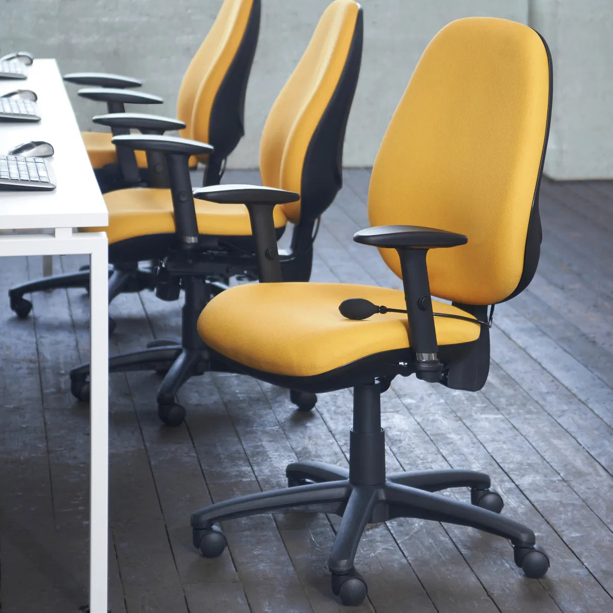 Row of yellow fabric task chairs with adjustable arms at white office desks